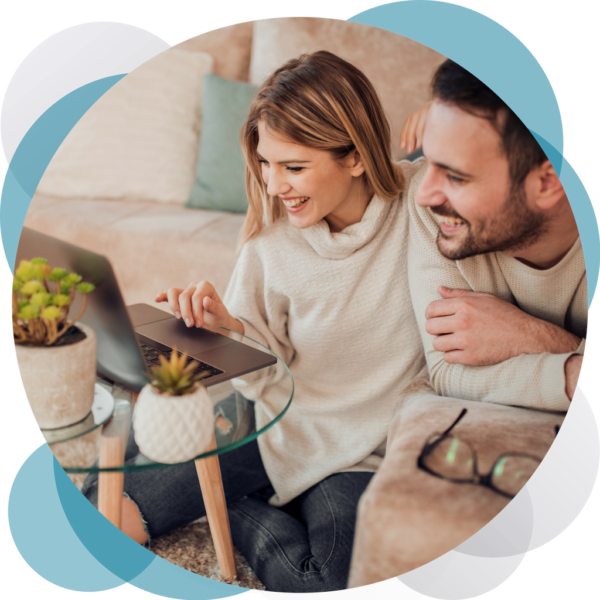 A man and woman sitting on the couch looking at a laptop.