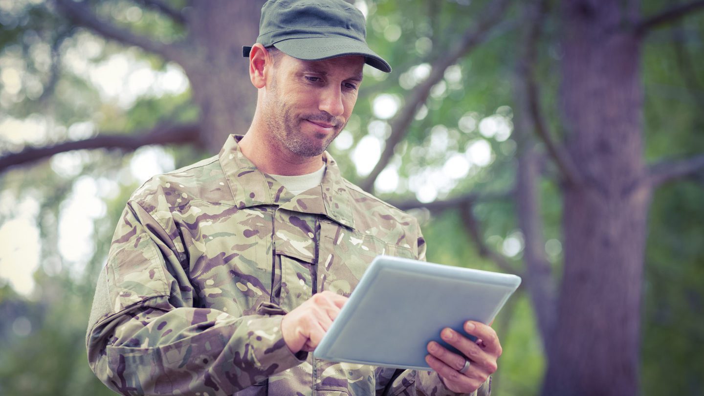A man in camouflage uniform holding an ipad.