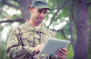 A man in camouflage uniform holding an ipad.