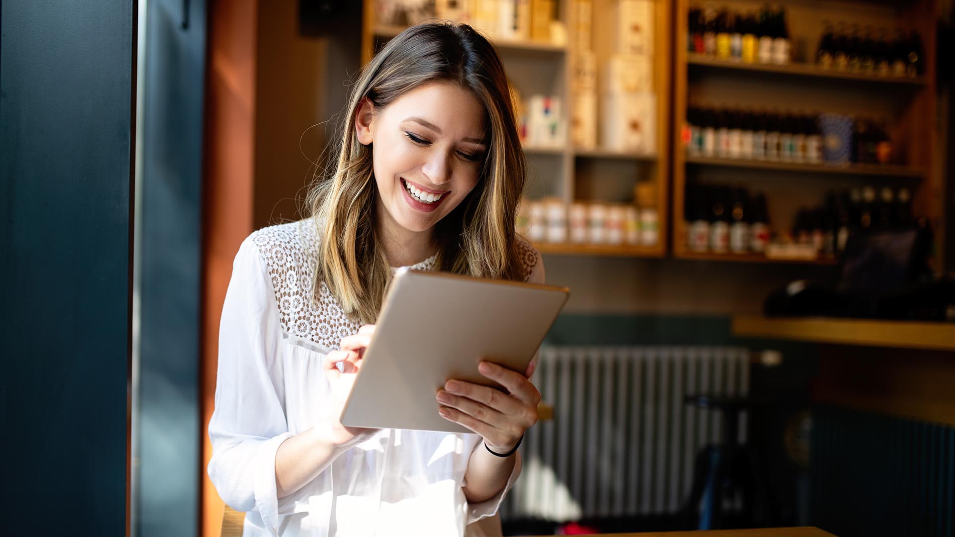 A woman is smiling while looking at her tablet.